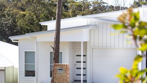 A modern two-story house with a garage, a brick column, and a tree in front.