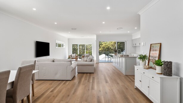 A modern kitchen with white cabinets, a dining area with a table and chairs, and a living room with a sofa and TV.