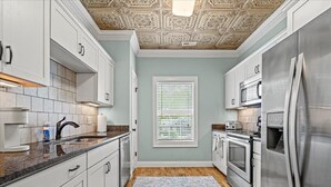 Una cocina con armarios blancos, electrodomésticos de acero inoxidable, un tapete estampado y un techo decorativo.