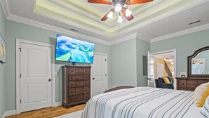 Un dormitorio con cama, cómoda, televisor y ventilador de techo.