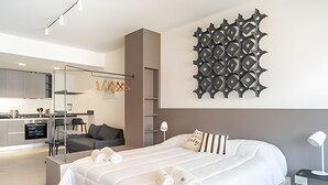 A modern bedroom with a large bed, a desk, and a kitchenette in the background. - Perfect Studio Amazing Location (Buenos Aires)
