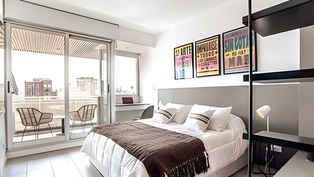 A modern bedroom with a large bed, a desk, and a balcony with chairs. - Perfect Studio Amazing Location (Buenos Aires)
