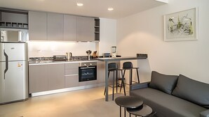 A modern kitchen with grey cabinets, a built-in oven, and a dining area with a grey sofa and two bar stools. - Perfect Studio Amazing Location (Buenos Aires)