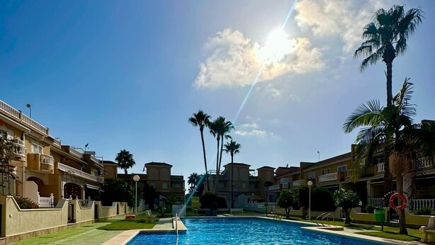 Una piscina rodeada de edificios con balcones, palmeras y un cielo despejado.