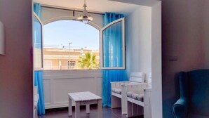 Una habitación con un ventanal grande, una mesa blanca, dos bancos blancos y una silla azul.