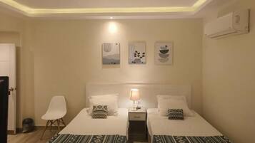Une chambre d’hôtel avec deux lits, une table de chevet avec une lampe, une chaise et des œuvres d’art murales.