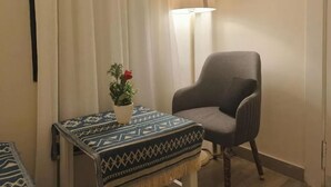 A room with a grey armchair, a small table with a patterned tablecloth, and a potted plant with a red flower. - Maria Pyramids House - Standard Double or Twin Room (Giza City)