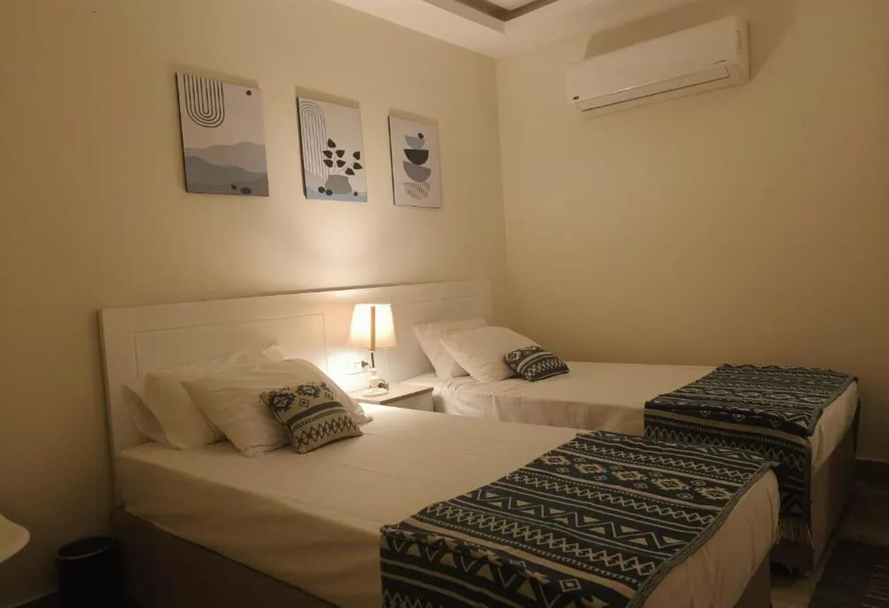 Ein Hotelzimmer mit zwei Betten, einem Nachttisch mit Lampe und Wandbildern.