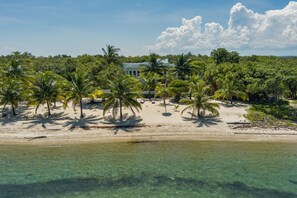 Une propriété située en bord de mer, avec un grand bâtiment entouré de palmiers et bordée par une eau turquoise et cristalline.