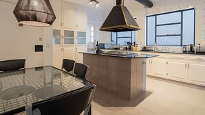 Moderni keittiö, jossa on keskeinen saareke, valkoiset kaapit ja suuri ikkuna, josta tulee runsaasti luonnonvaloa.
