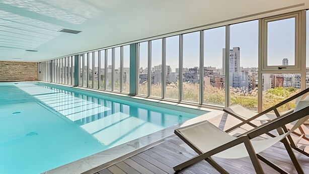 Une piscine intérieure avec vue sur la ville, de grandes fenêtres et un plancher en bois.