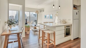 Une cuisine moderne dotée d’un îlot central, de tabourets en bois et d’un coin repas avec une table et des chaises.