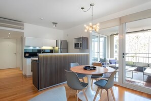 A modern kitchen with a central island, a dining area with a round table and chairs, and a balcony with outdoor seating. - Great 2BR with Heated Rooftop Pool, Gym & Hot Tub (Buenos Aires)