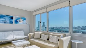 A modern living room with a large window, a sofa, a coffee table, and a side table. - Luxury 2BR Apartment with Pool, Gym & Spa (Buenos Aires)
