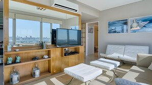A modern living room with a large TV, white sofas, and a city view. - Luxury 2BR Apartment with Pool, Gym & Spa (Buenos Aires)