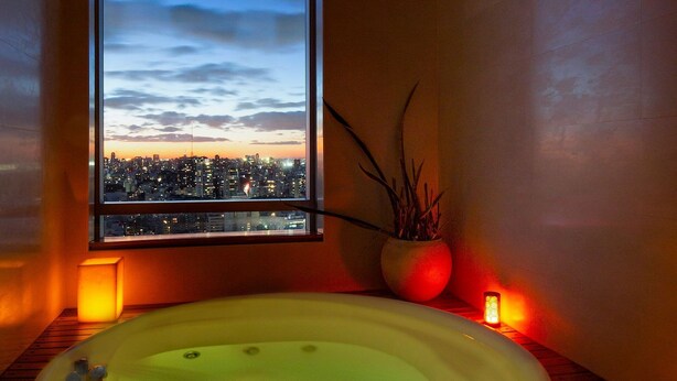 A room with a large window, a hot tub, a potted plant, and a candle. - Luxury 2BR Apartment with Pool, Gym & Spa (Buenos Aires)