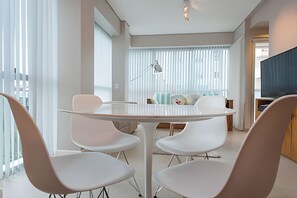 A modern living room with a dining area, featuring a round table with four chairs, a sofa set, and a television.