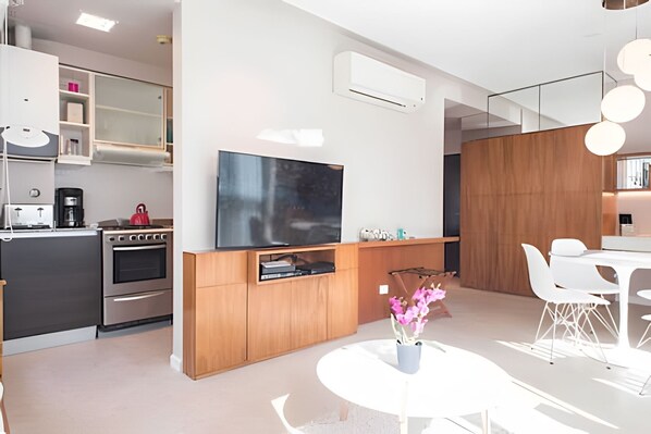 A modern kitchen with a built-in oven and stove, a dining area with a white table and chairs, and a flat-screen TV mounted on the wall.