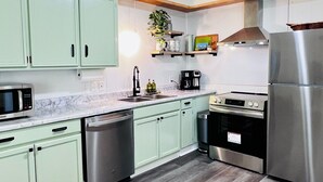 Una cocina moderna con armarios verde claro, electrodomésticos de acero inoxidable y suelo de madera.