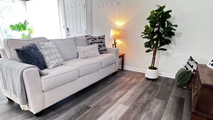 Una sala de estar con un sofá gris, cojines estampados, una lámpara de pie y una planta en maceta.
