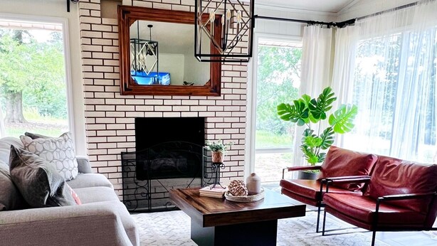 Una sala de estar con chimenea de ladrillo, un sofá, un sillón de cuero rojo y una mesa de centro.