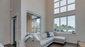 Una sala de estar moderna con un sofá modular, ventanas amplias y suelo de madera.