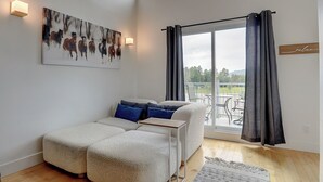 A modern living room with a sectional sofa, a painting of horses, a balcony with a view, and a 'relax' sign. - Condotel (Magog)