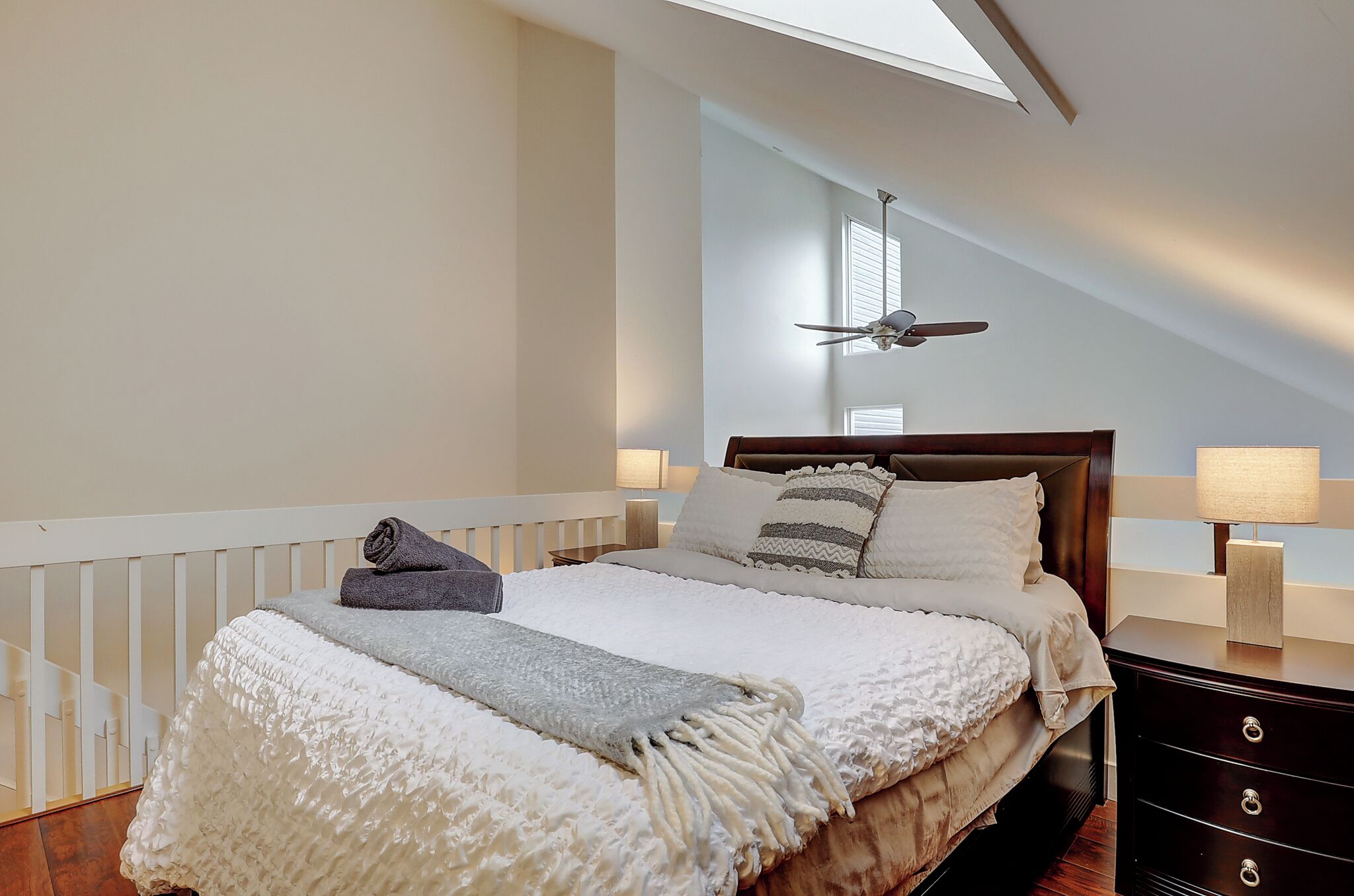 A bedroom with a large bed, a ceiling fan, and a nightstand with a lamp.