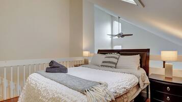 A bedroom with a large bed, a ceiling fan, and a nightstand with a lamp.