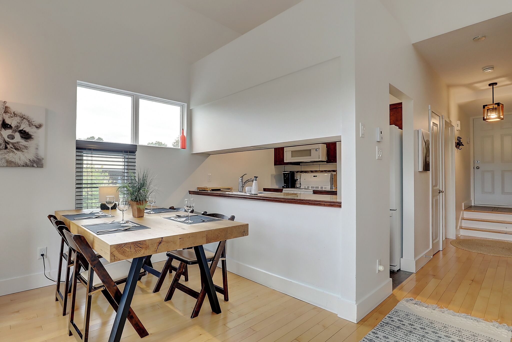 Una cocina moderna con alacenas blancas, microondas y pileta. Hay un comedor con una mesa y sillas de madera.