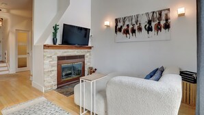 A modern living room with a fireplace, a flat-screen TV, and a large painting of horses. - Condotel (Magog)