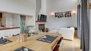 A dining area with a wooden table set for four, a fireplace, and a mounted television. - Condotel (Magog)