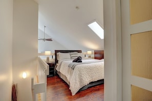 A bedroom with a sloped ceiling, a bed with a white bedspread, two bedside lamps, and a ceiling fan.
