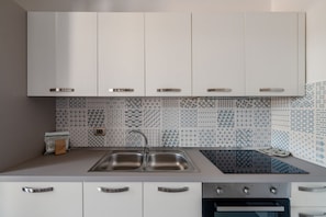 A modern kitchen with white cabinets, a stainless steel sink, patterned backsplash, and a built-in oven. - La Dimora di Nobile II by Rentbeat (Carovigno)