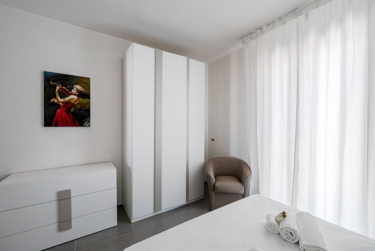 Una habitación de hotel moderna con una cama, una silla, un armario y un cuadro en la pared.