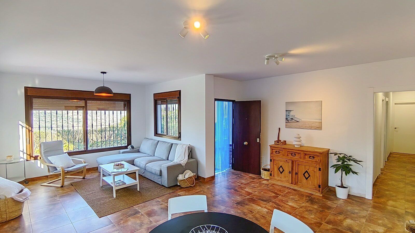 A spacious living area with a sofa, a coffee table, and a chair. There is a wooden cabinet and a potted plant.
