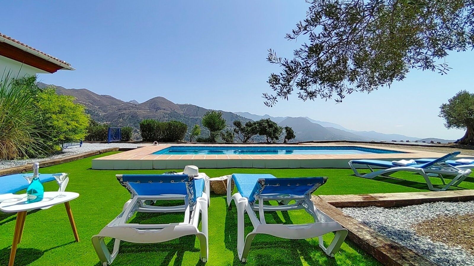 A pool area with lounge chairs and a table, surrounded by a well-maintained lawn and trees.