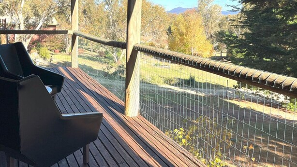 Une terrasse en bois avec un banc et une vue sur un espace clos, agrémenté d’arbres et avec une montagne en arrière-plan.