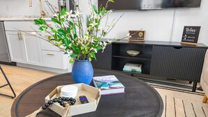 Una sala de estar moderna con una mesa redonda, un jarrón con flores, un libro y un control remoto.
