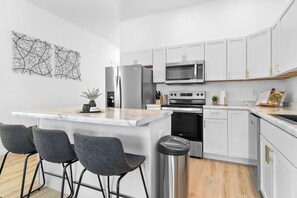 A modern kitchen with white cabinets, stainless steel appliances, and a marble countertop. - Uptown Haven: Stylish Stay Near Downtown with Bikes and Firepit near Downtown (Evansville)