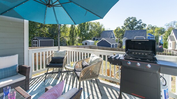 Un patio techado al aire libre con una parrilla, mobiliario de mimbre y vista a casas vecinas.