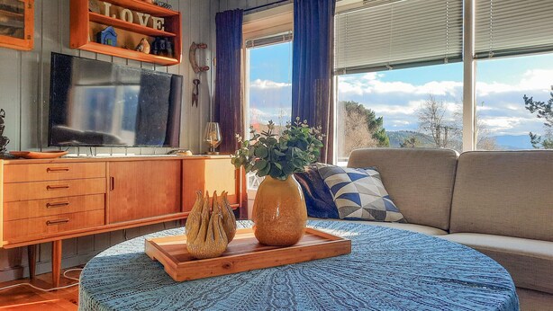 A cozy living room with a wooden TV stand, a sofa, and a large window offering a scenic view.