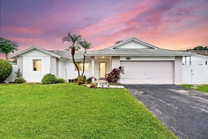 A single-story house with a garage, a well-maintained lawn, and a variety of plants.