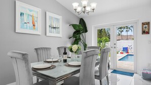 A dining area with a glass table, grey upholstered chairs, and two framed paintings on the wall. - Family Favorite-Heated Pool/2 Kings/Everglades (Homestead)