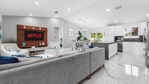 A modern living room with a grey sofa, striped armchairs, and a flat-screen TV mounted on a wooden wall. - Family Favorite-Heated Pool/2 Kings/Everglades (Homestead)