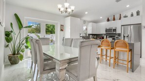 A modern kitchen with white cabinets, a stainless steel refrigerator, and a dining area with a glass table and chairs. - Family Favorite-Heated Pool/2 Kings/Everglades (Homestead)