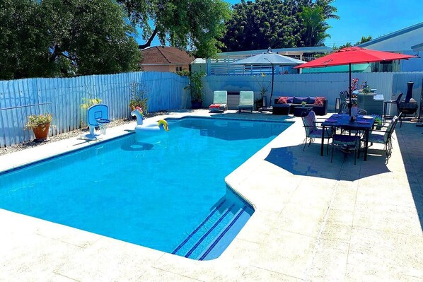 A backyard with a swimming pool, patio furniture, and a barbecue grill.