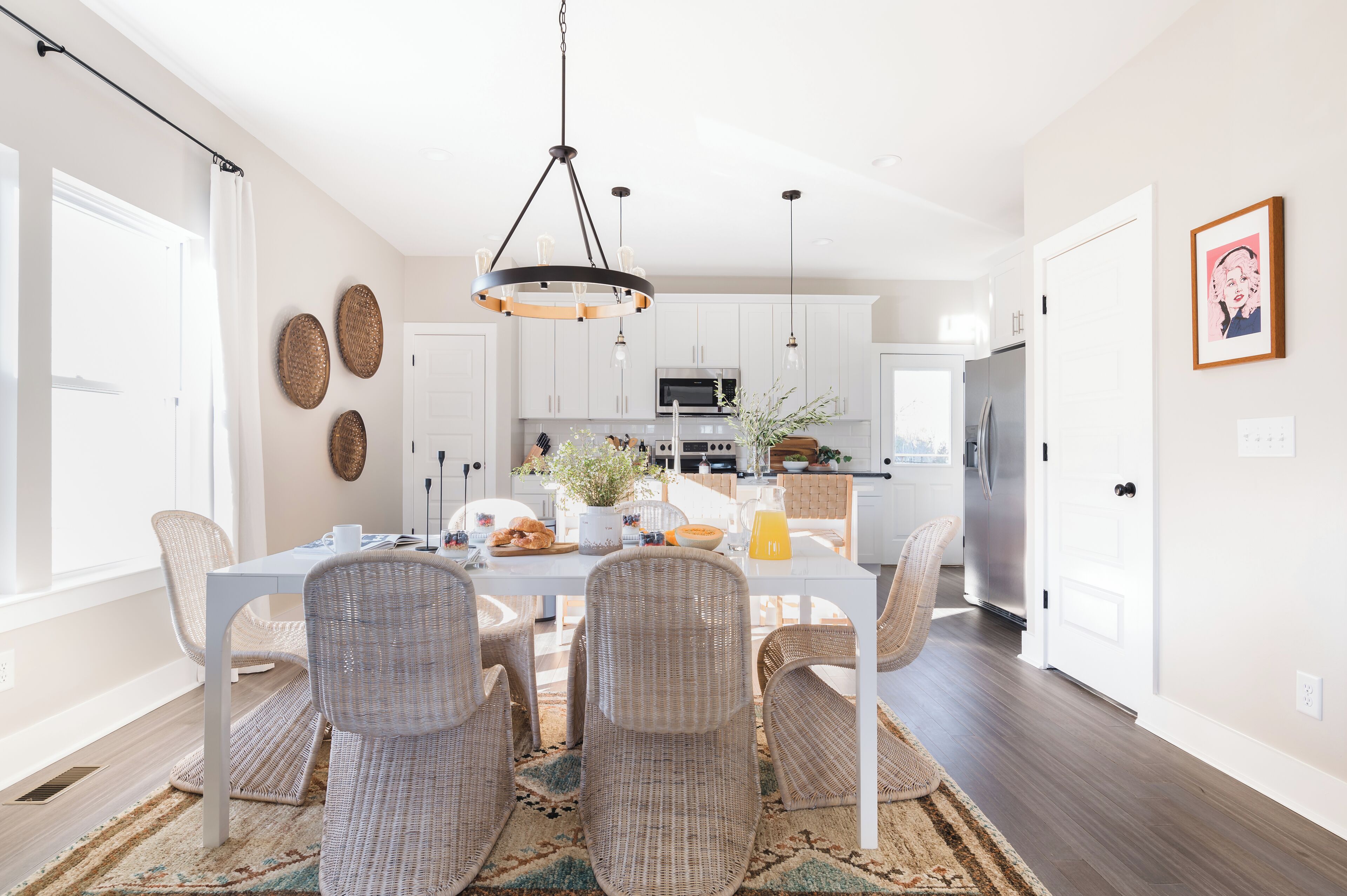 A modern kitchen with white cabinets, stainless steel appliances, and a dining area with wicker chairs and a white table.