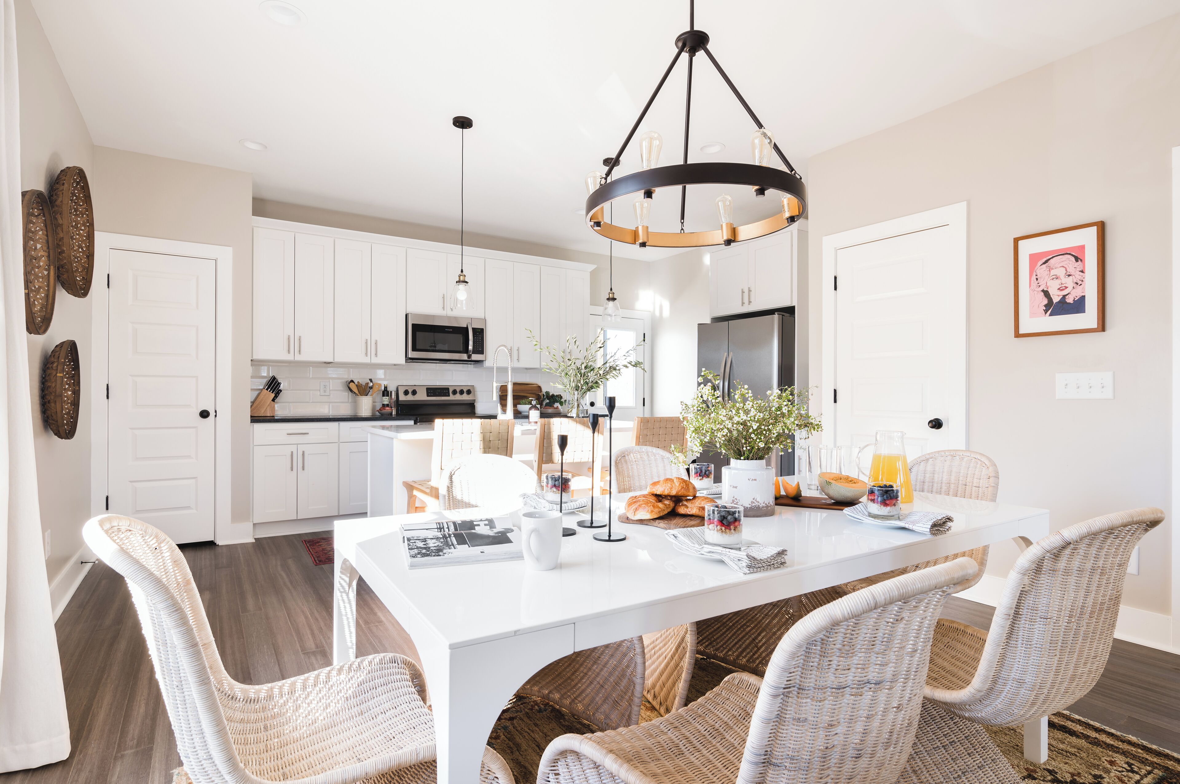 Una cocina moderna con armarios blancos, electrodomésticos de acero inoxidable y un comedor con sillas de mimbre y una mesa blanca.