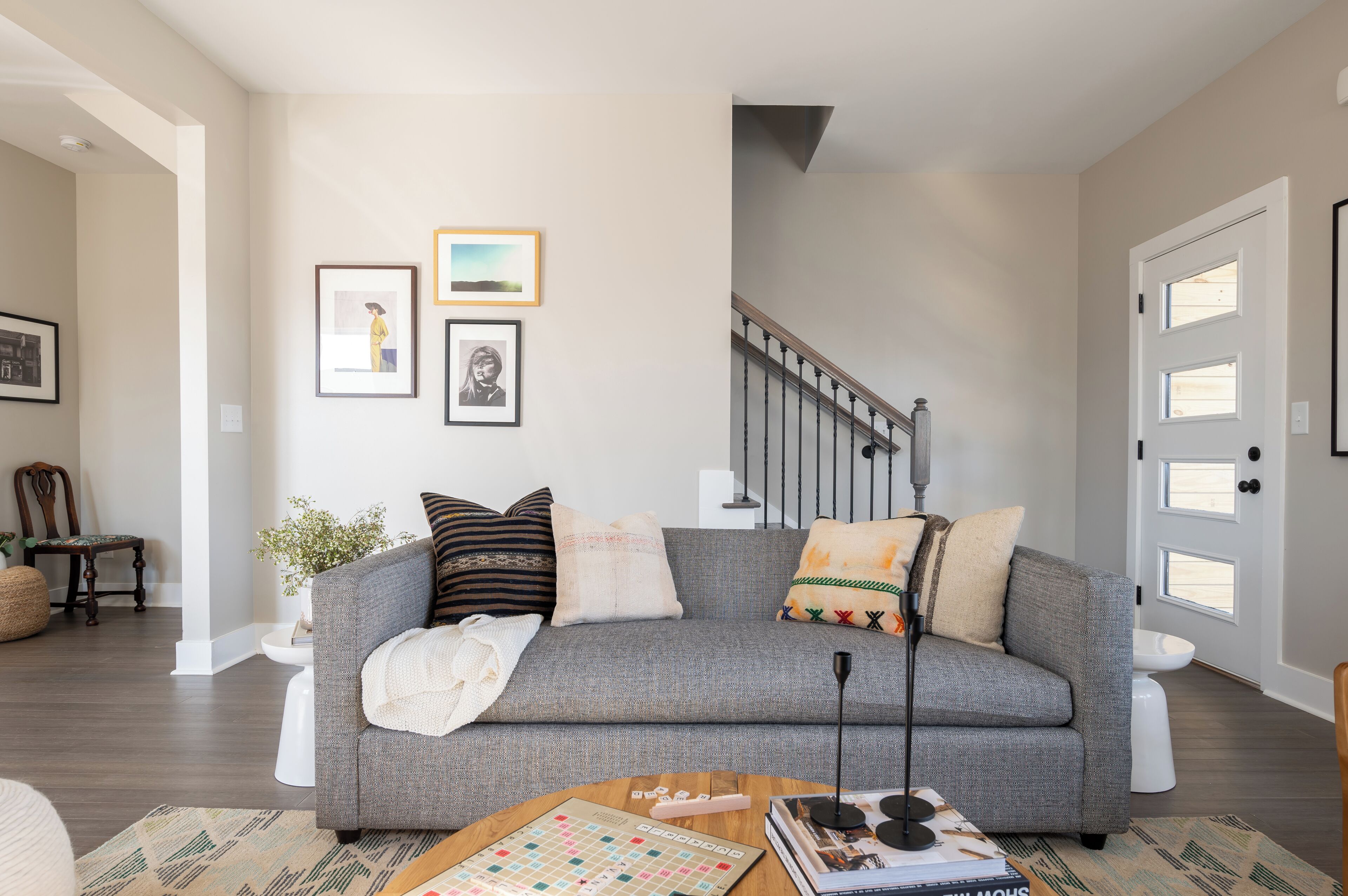 A living room with a grey sofa, a coffee table with books and a board game, a staircase, and a door with windows.